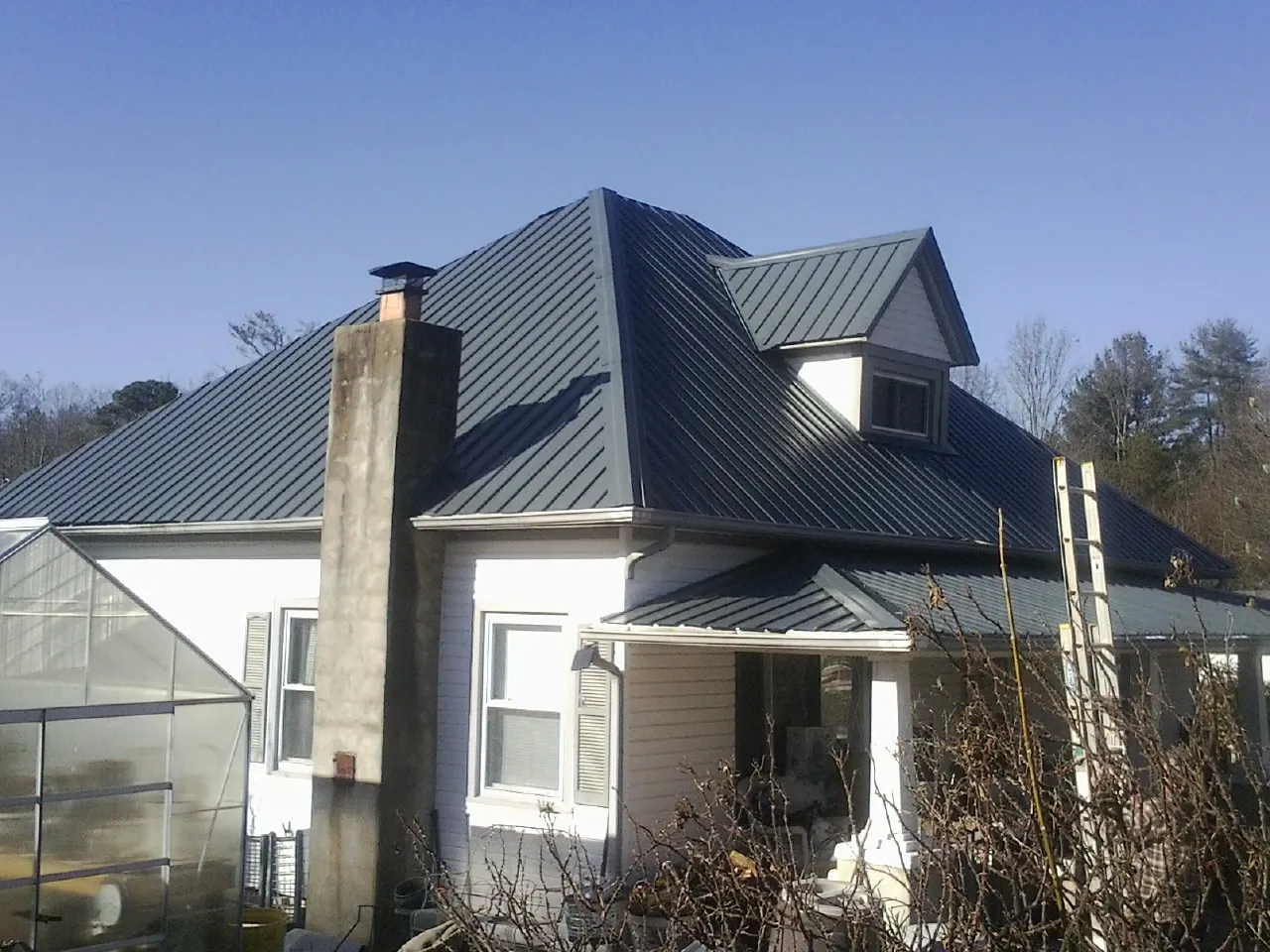 Dark blue standing seam metal roof on a white farmhouse with dormer — Slate & Tile Roof Repair by Roofing Brothers in Hewlett