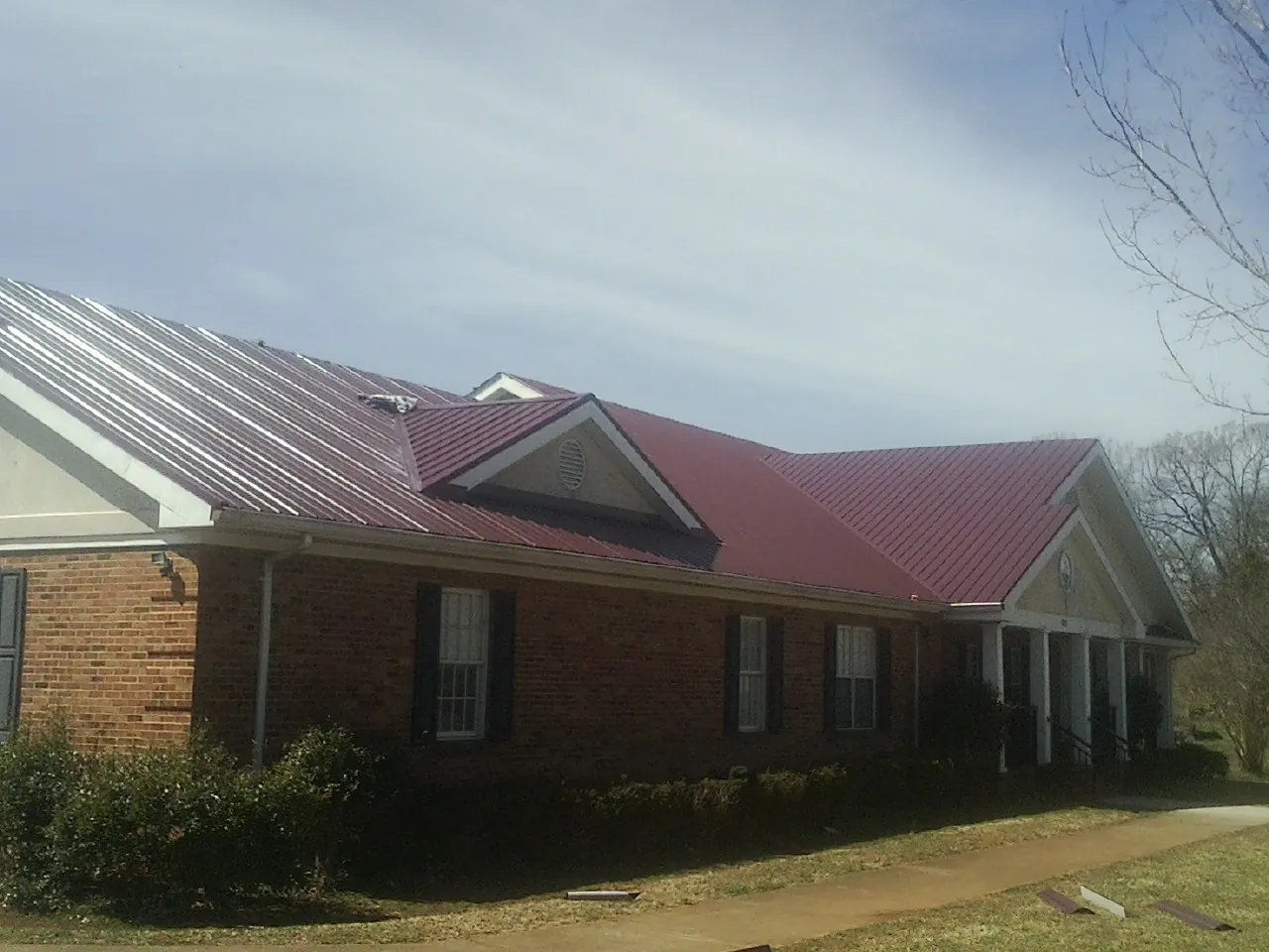 Red metal roof with gabled entries on a long brick building, from a Hail Damage Roof Repair job in Hewlett