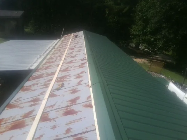 Old rusted panels beside newly installed green metal roofing — Wind Damage Roof Repair by Roofing Brothers in Hewlett