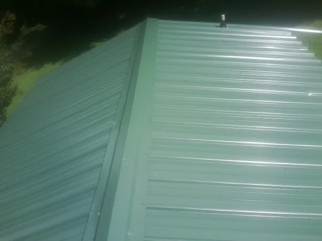 New green metal panels meeting at the ridge of a roof — Flat Roof Repair work by our crew in Hewlett