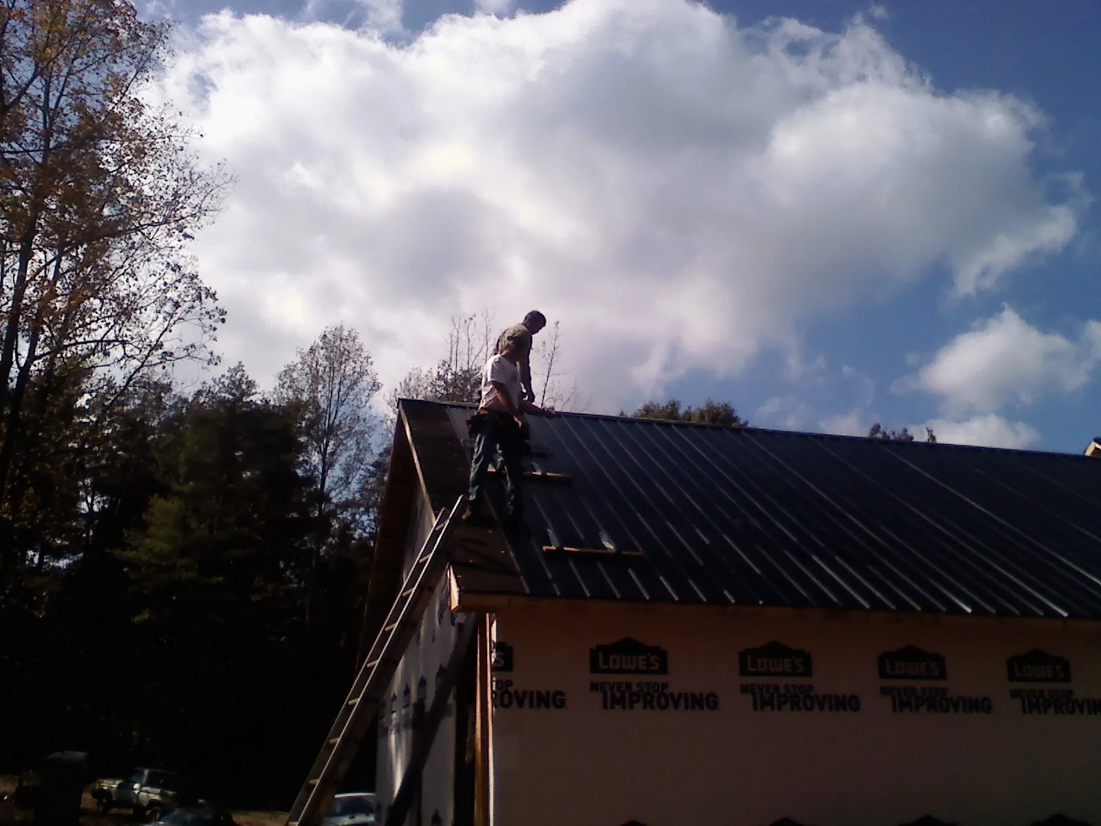 Roofer fastening dark metal panels high against a cloudy sky, from a Roof Inspection job in Hewlett
