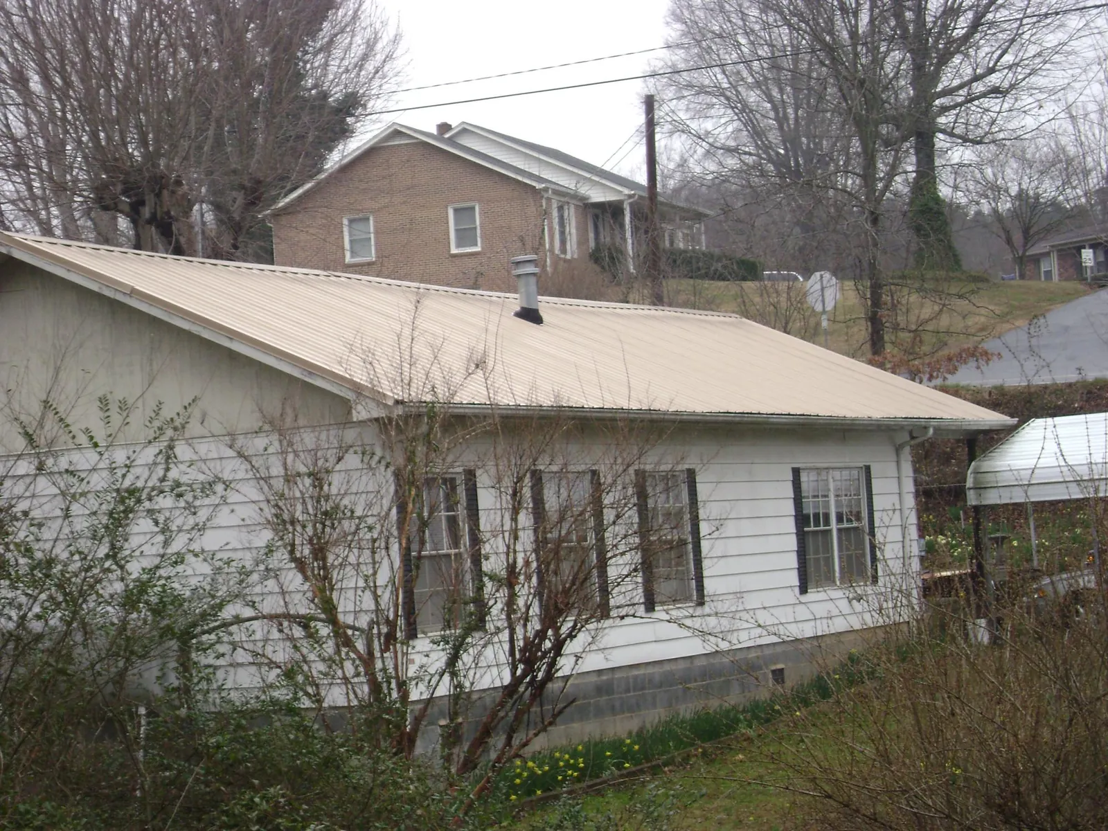 Tan metal roof on a white sided house set into a hillside — Commercial Roofing by Roofing Brothers in Hewlett
