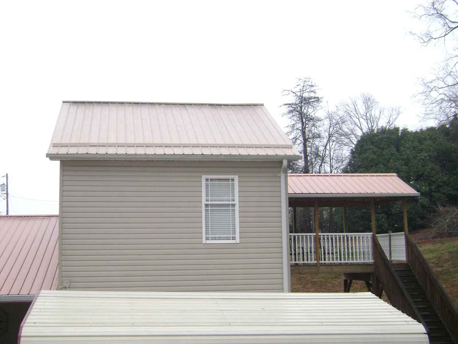 Tan metal roofs on a two story addition and attached porch, from a Roof Replacement job in Hewlett