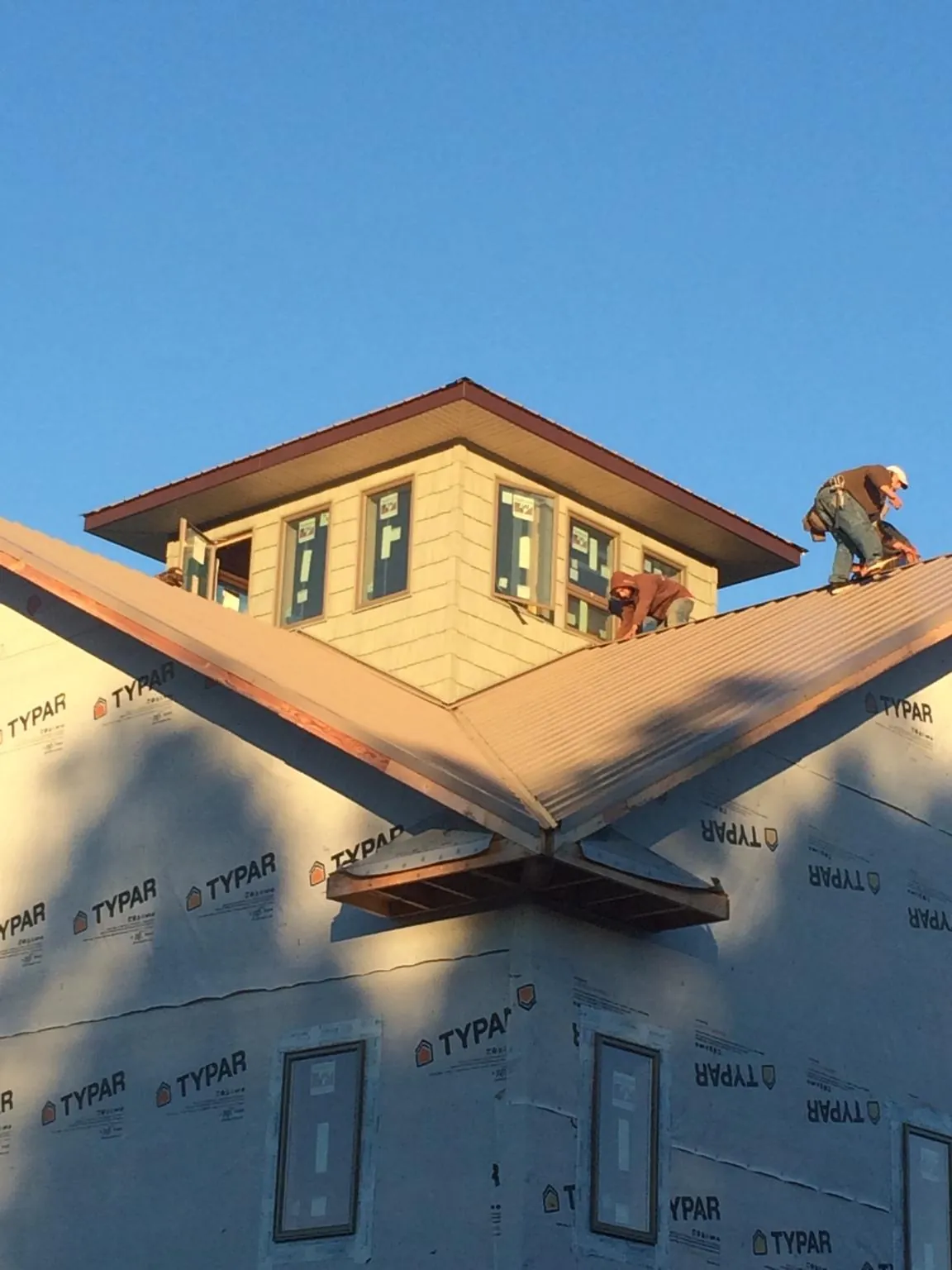 Roofers working around a rooftop cupola on a new metal roof at sunset — Roof Waterproofing in Hewlett by Roofing Brothers